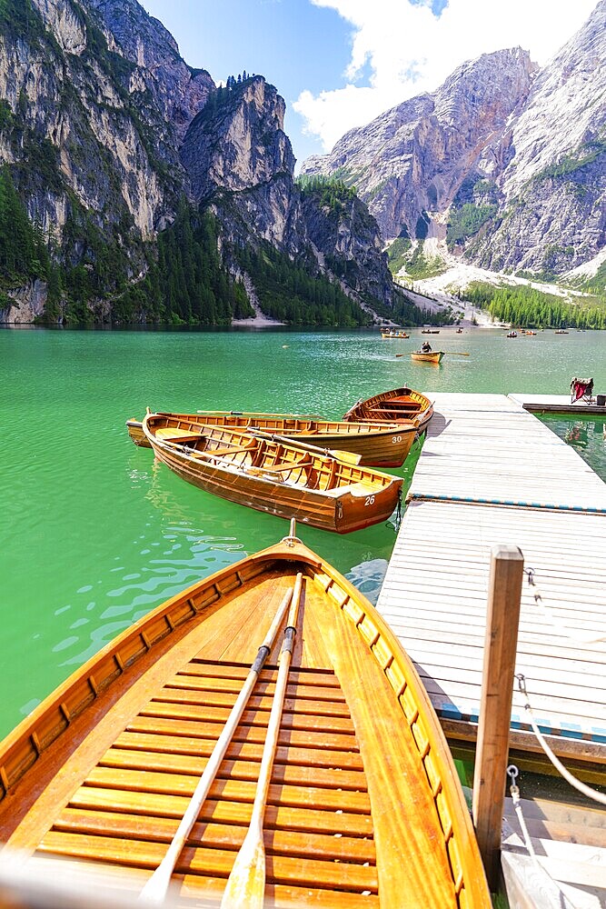 Several wooden boats are moored to a jetty on a calm, emerald-green mountain lake, Lake Braies, South Tyrol, Dolomites, Italy