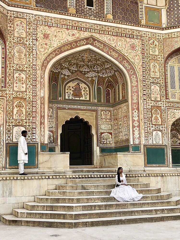 Decorated palace entrance with stairs and two people in traditional dress in a historic building, Amber Fort, Jaipur, Rajasthan, India