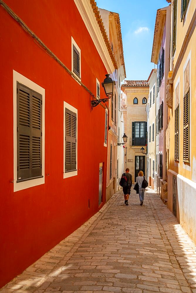 View of couple walking down pastel coloured street in historic centre, Ciutadella, Memorca, Balearic Islands, Spain, Europe