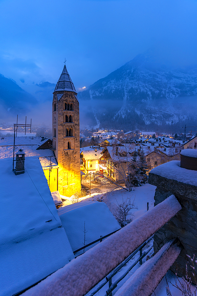 View of Church of Saint Pantalon and the snow covered town centre and mountainous background in winter at dusk, Courmayeur, Aosta Valley, Italy, Europe