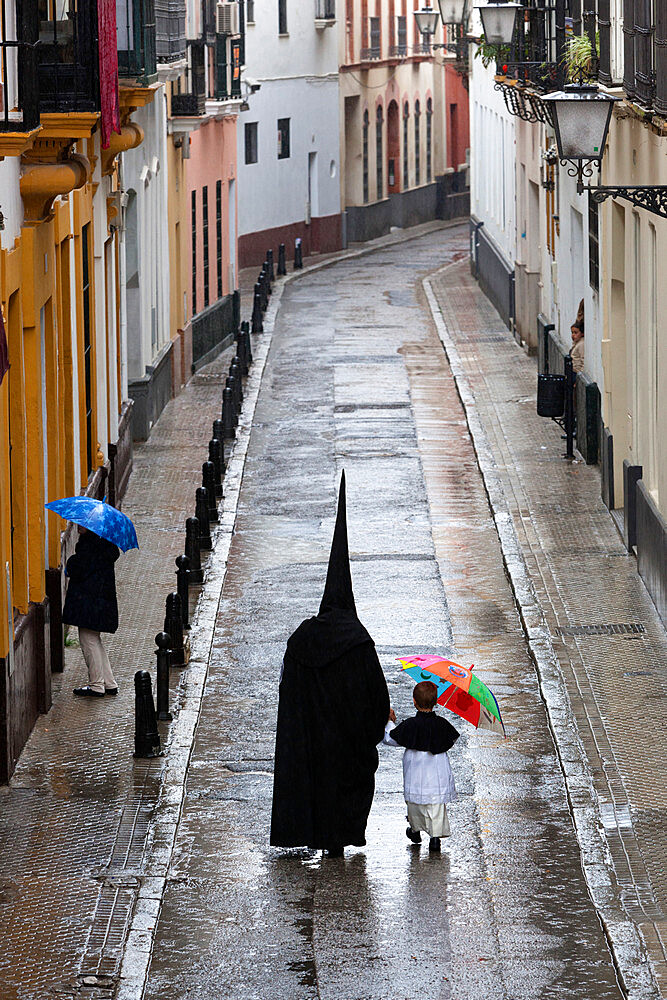 Penitents during Semana Santa (Holy Week) along rainy street, Seville, Andalucia, Spain, Europe