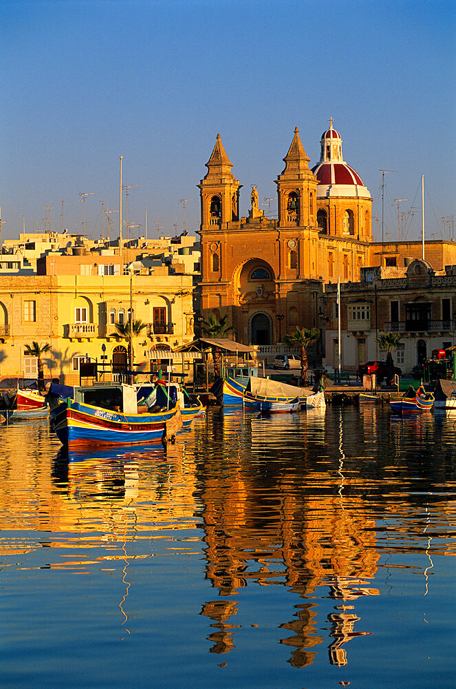 Harbour with Luzzu fishing boats and Marsaxlokk Parish Church at sunrise, Marsaxlokk, Malta, Mediterranean, Europe