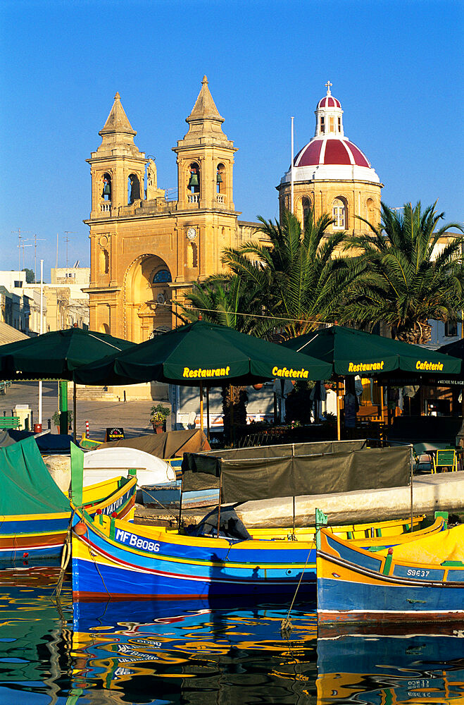 Harbour with Luzzu fishing boats and Marsaxlokk Parish Church, Marsaxlokk, Malta, Mediterranean, Europe