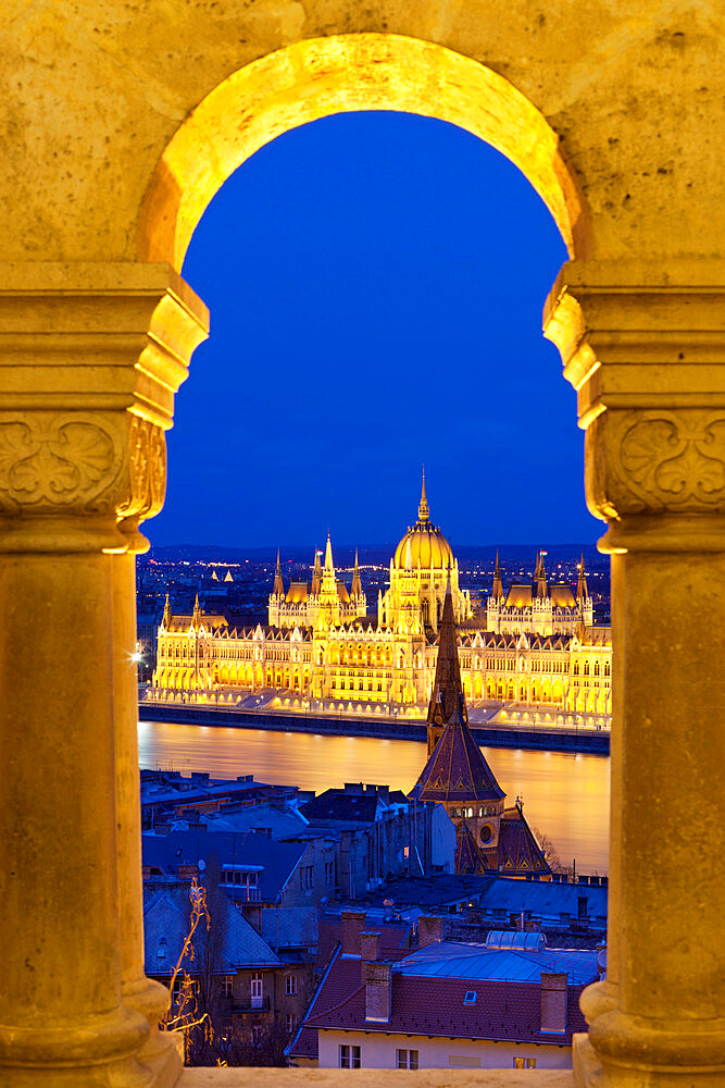 Parliament (Orszaghaz) through arches of Fishermen's Bastion (Halaszbastya) at dusk, UNESCO World Heritage Site, Budapest, Hungary, Europe