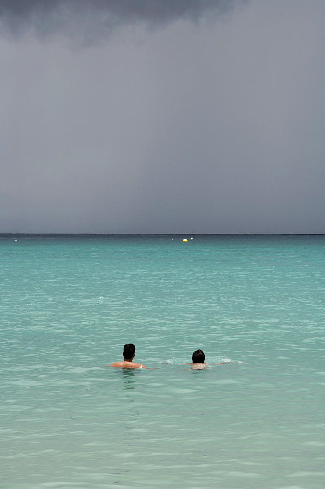 Man and woman in sea with grey storm clouds behind, Beau Vallon beach, Mahe, Seychelles, Indian Ocean