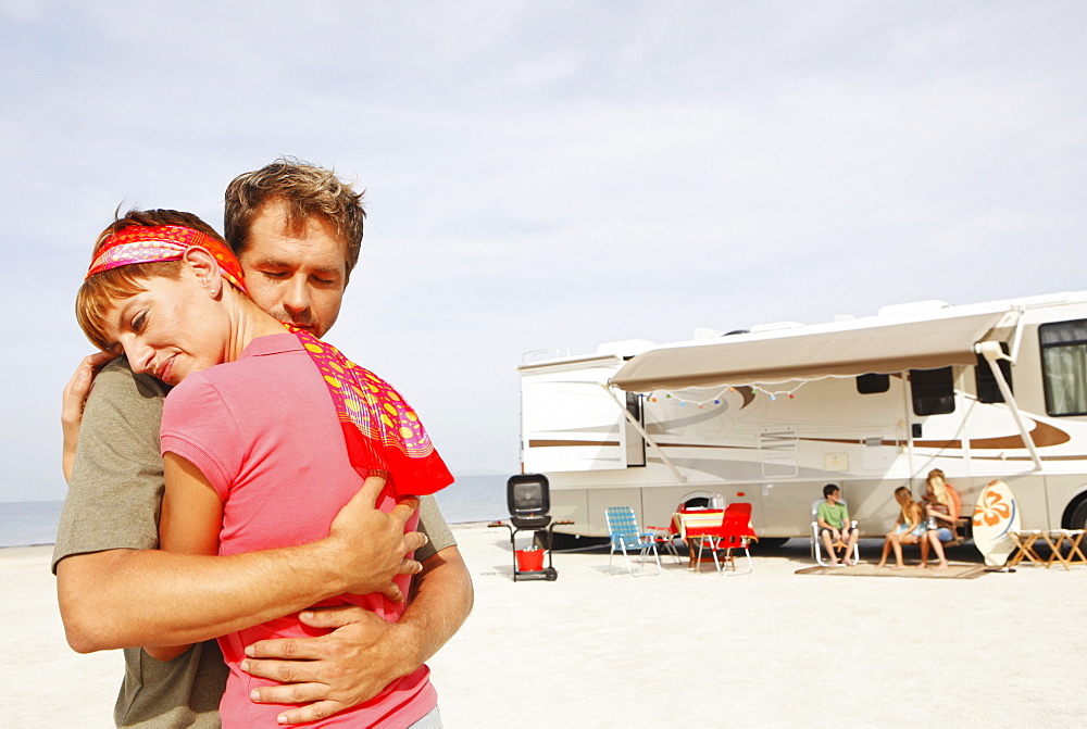 Couple hugging on beach with motor home in background