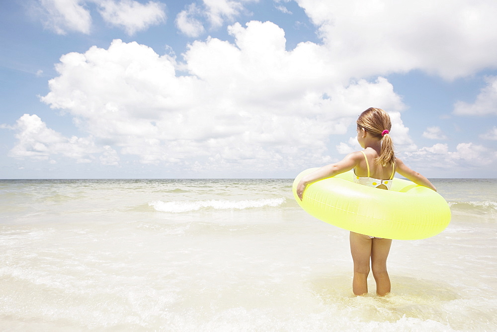 Girl carrying inflatable ring into ocean