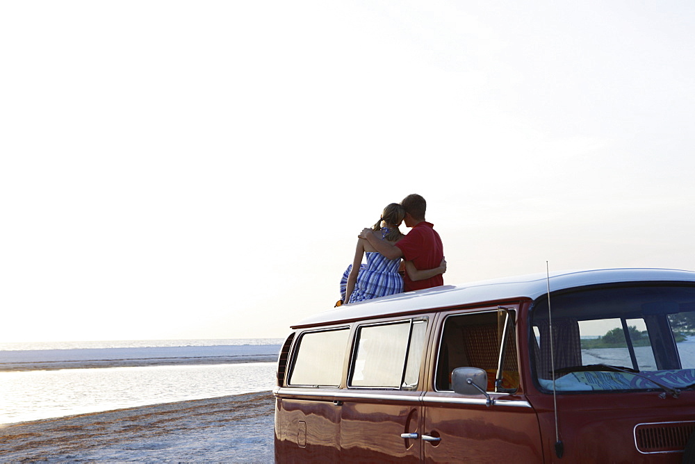 Couple watching ocean sunset from top of van