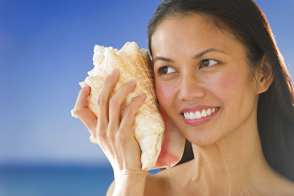 USA, New Jersey, Jersey City, Woman listening to conch shell near sea