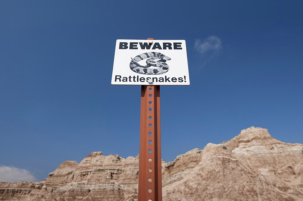 USA, South Dakota, Badlands National Park, Rattlesnake warning sign against sky, mountain in background