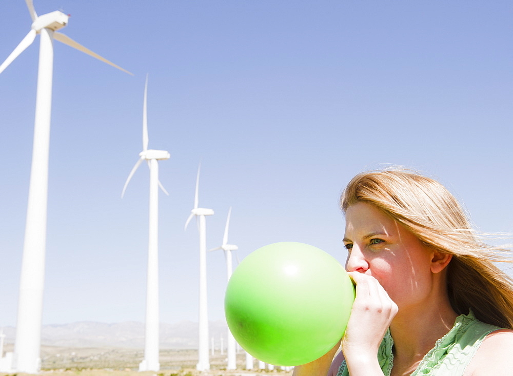 USA, California, Palm Springs, Coachella Valley, San Gorgonio Pass, Woman blowing green balloon with wind turbines in background