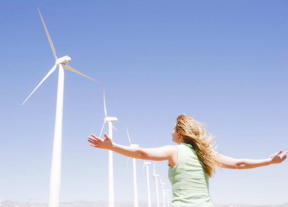 USA, California, Palm Springs, Coachella Valley, San Gorgonio Pass, Rear view of woman stretching arms and looking at wind turbines 