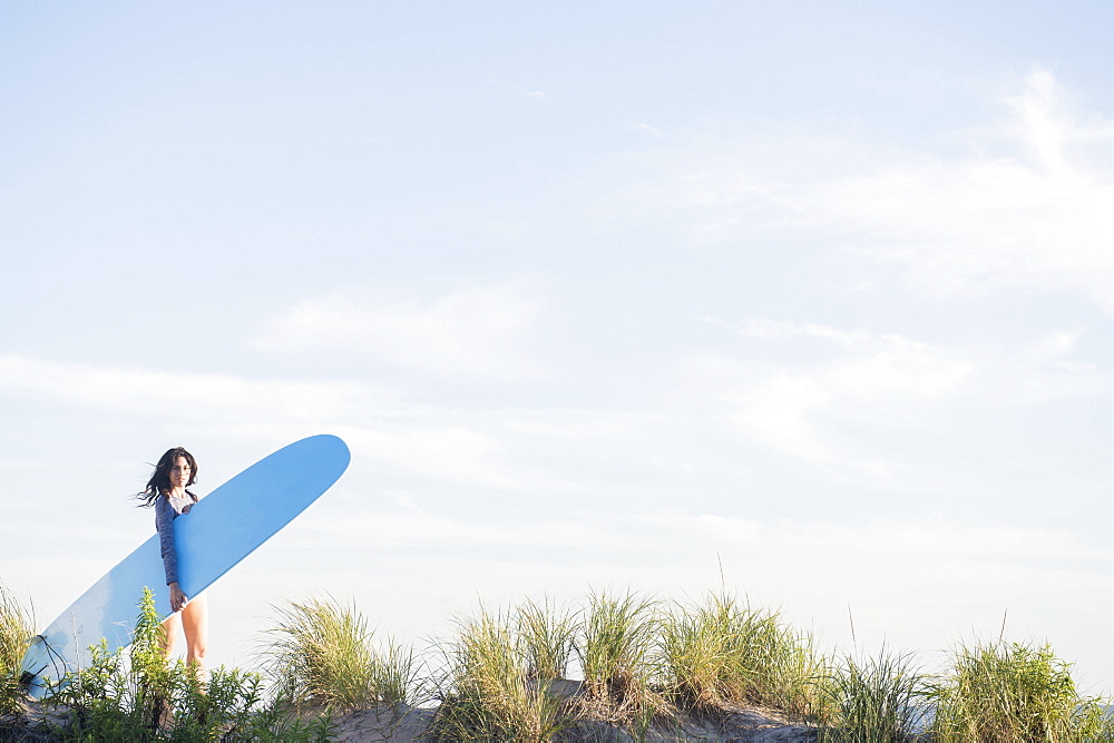 Female surfer walking on beach, Rockaway Beach, New York