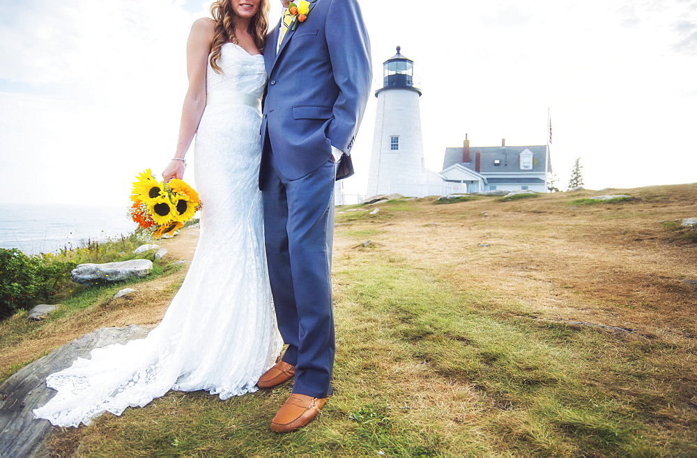 Low section of married couple, lighthouse in background, USA, Maine, Bristol 