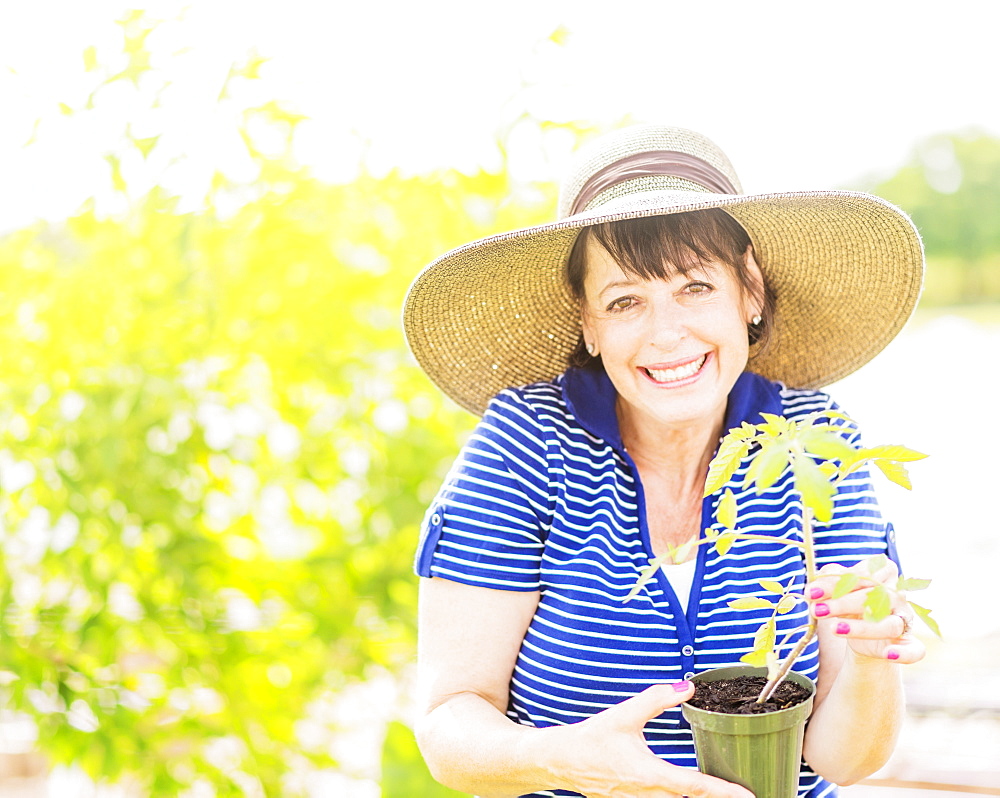 Portrait of smiling woman holding potted plant in garden