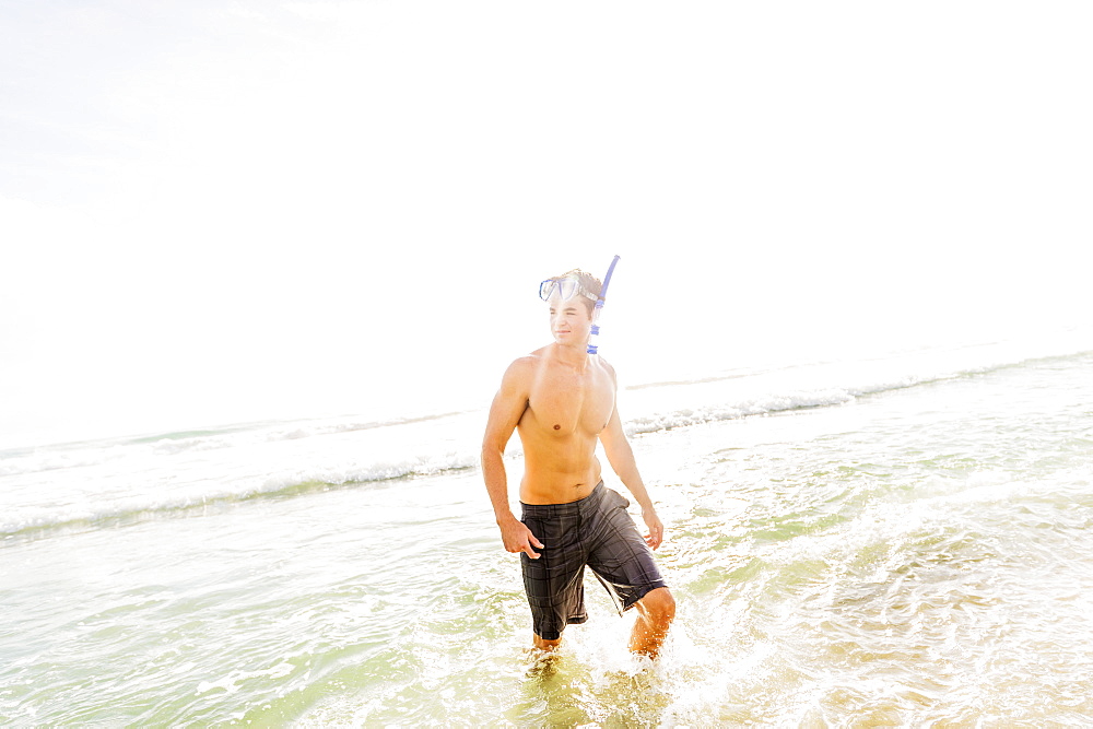 Portrait of young man walking in surf wearing scuba mask and snorkel, Jupiter, Florida