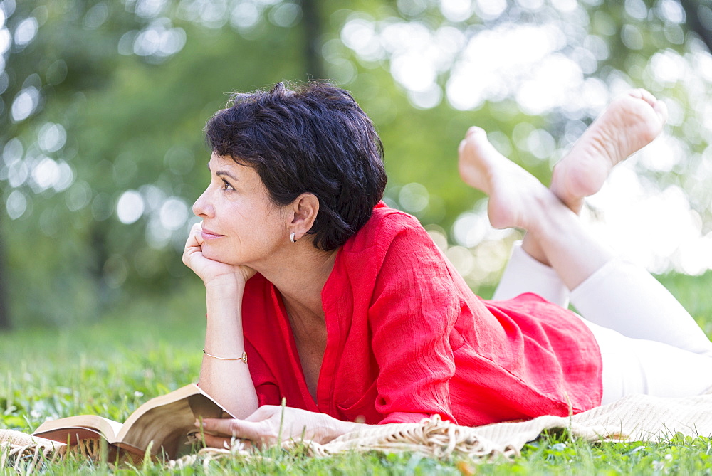 Mature woman lying on grass and reading book