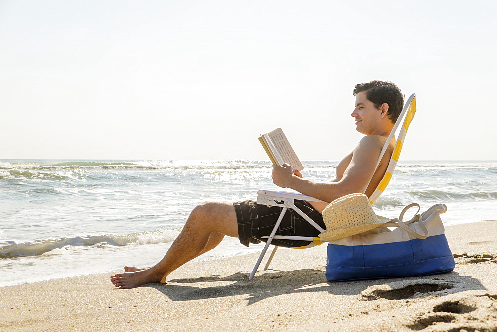 Side view of man sitting on deckchair and reading book, Palm Beach, Florida