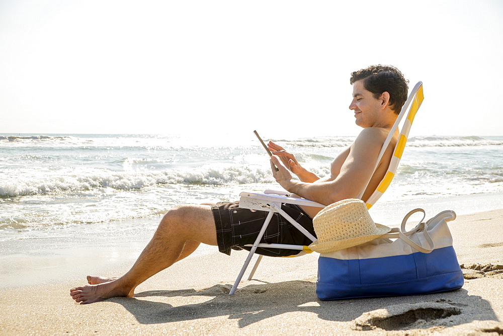 Side view of man sitting on deckchair and using digital tablet, Palm Beach, Florida