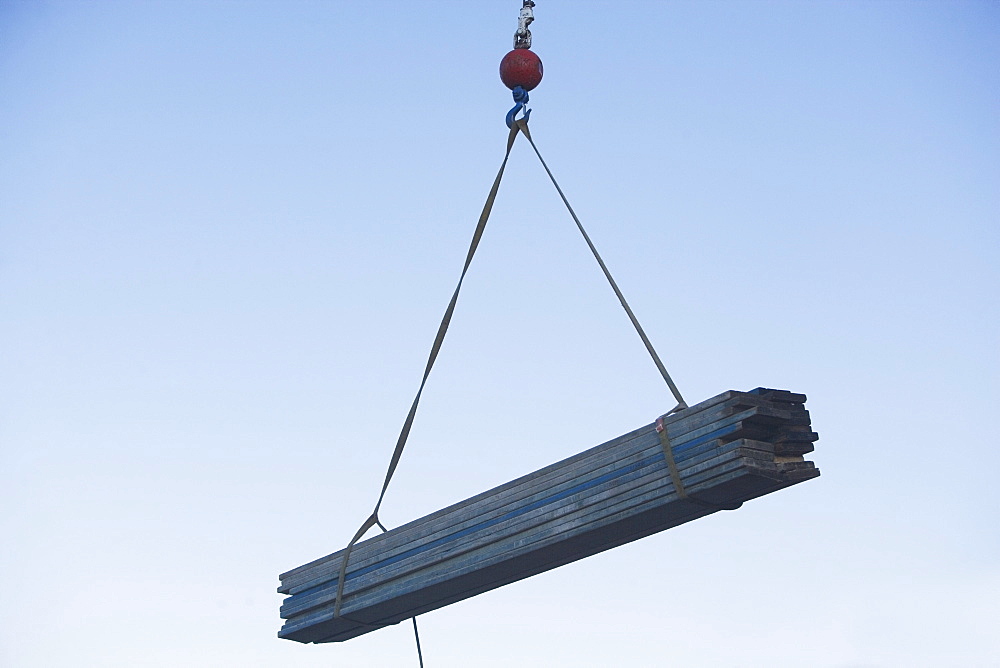 Mid-air view at crane's hook lifting wooden planks