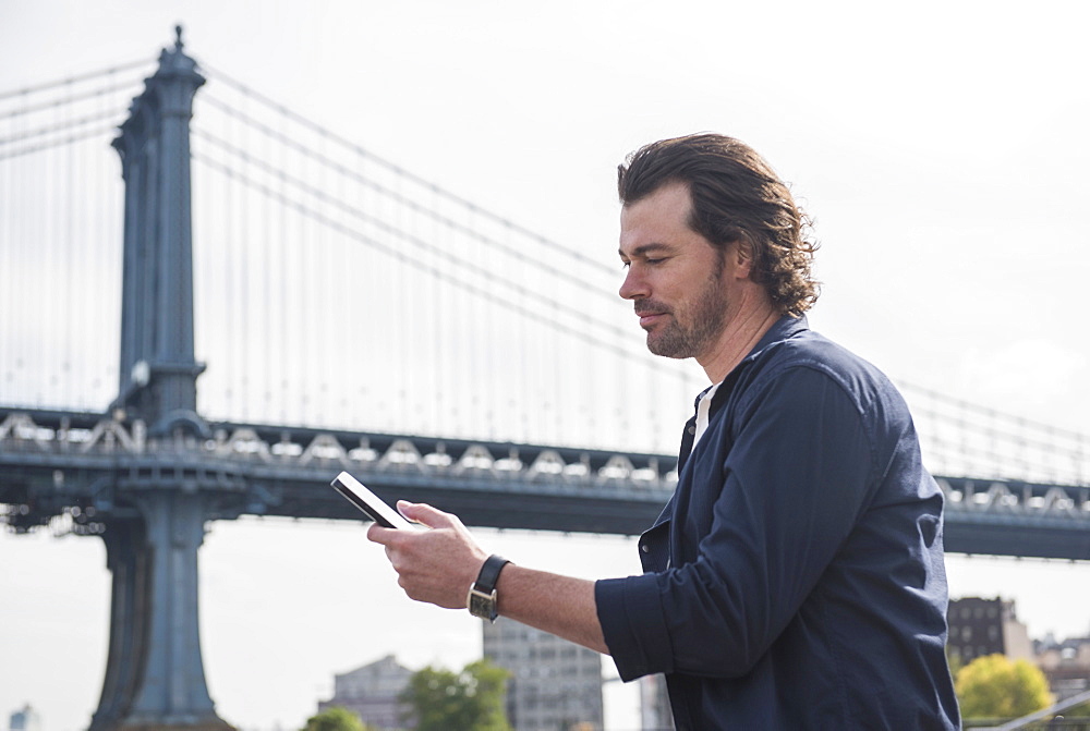 Man using tablet pc, Manhattan Bridge in background, Brooklyn, New York