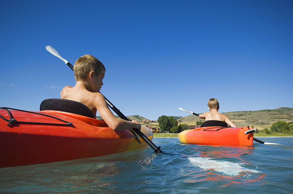 Brothers paddling in canoes on lake, Utah, United States