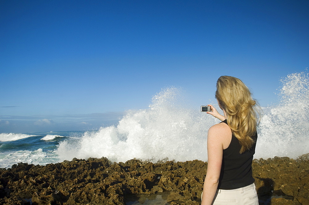 Woman taking photograph of ocean, Oahu, Hawaii, United States