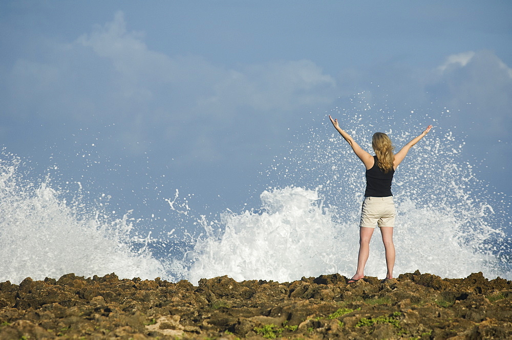 Woman with arms raised in front of ocean, Oahu, Hawaii, United States