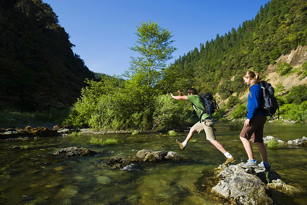 Hikers jumping across river on rocks