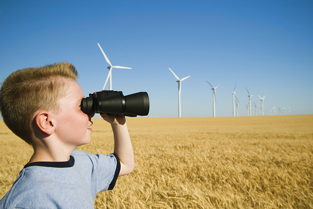 Boy on wind farm looking through binoculars