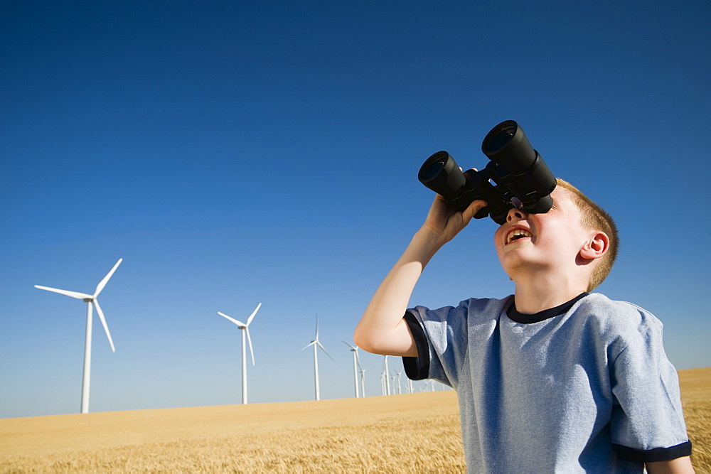 Boy on wind farm looking through binoculars