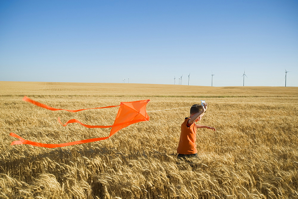 Boy running with kite on wind farm