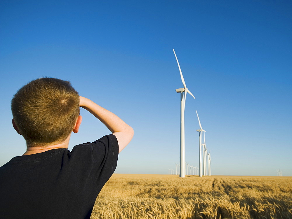 Boy looking up at windmills on wind farm