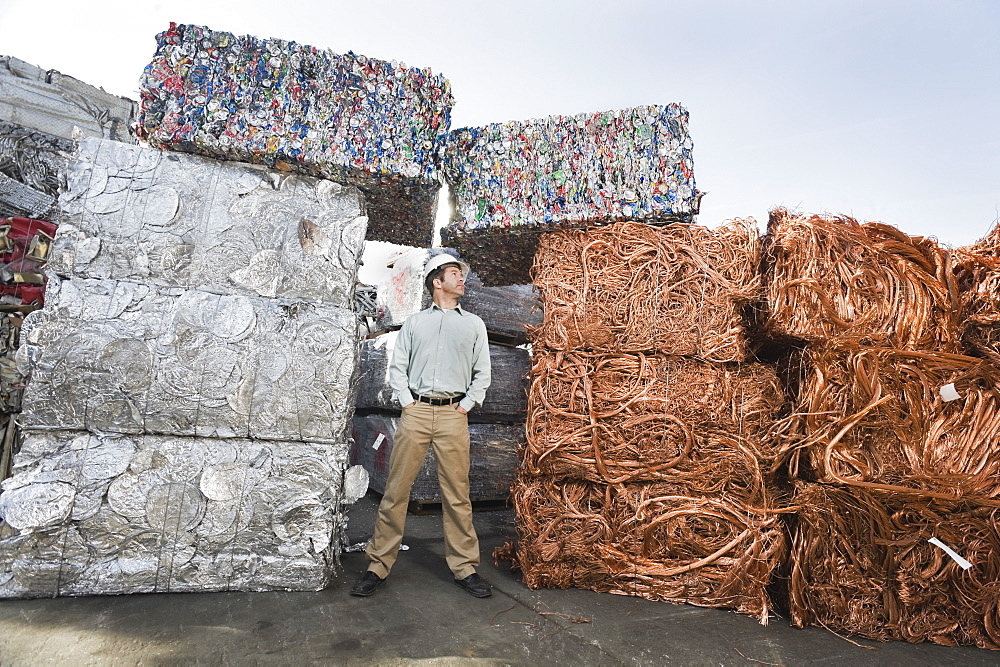 Worker standing beside stacks of recycled material