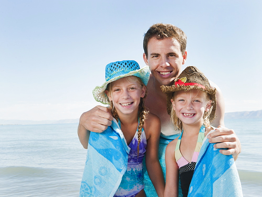 Portrait of girls (6-7,8-9) wrapped in towel on beach with their father