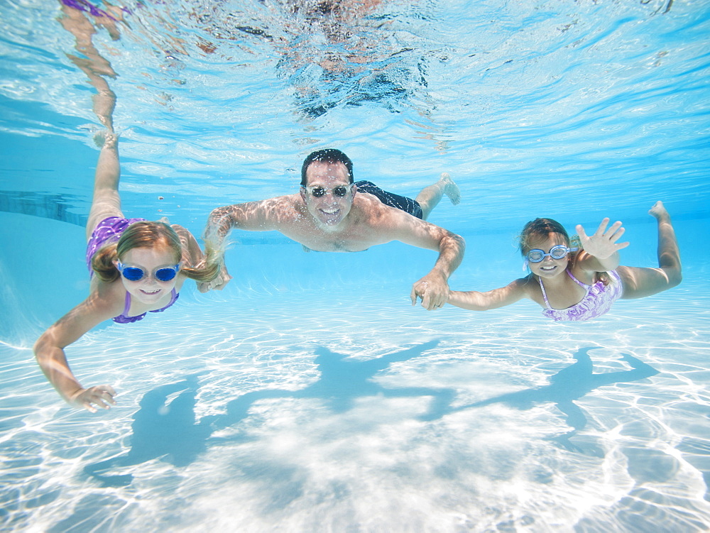 Father with two daughters (6-7,8-9) swimming underwater