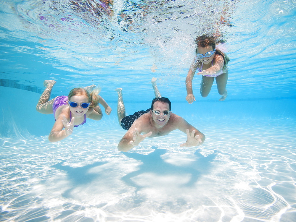 Father with two daughters (6-7,8-9) swimming underwater