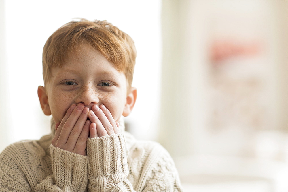 Portrait of boy (6-7) with hands covering mouth