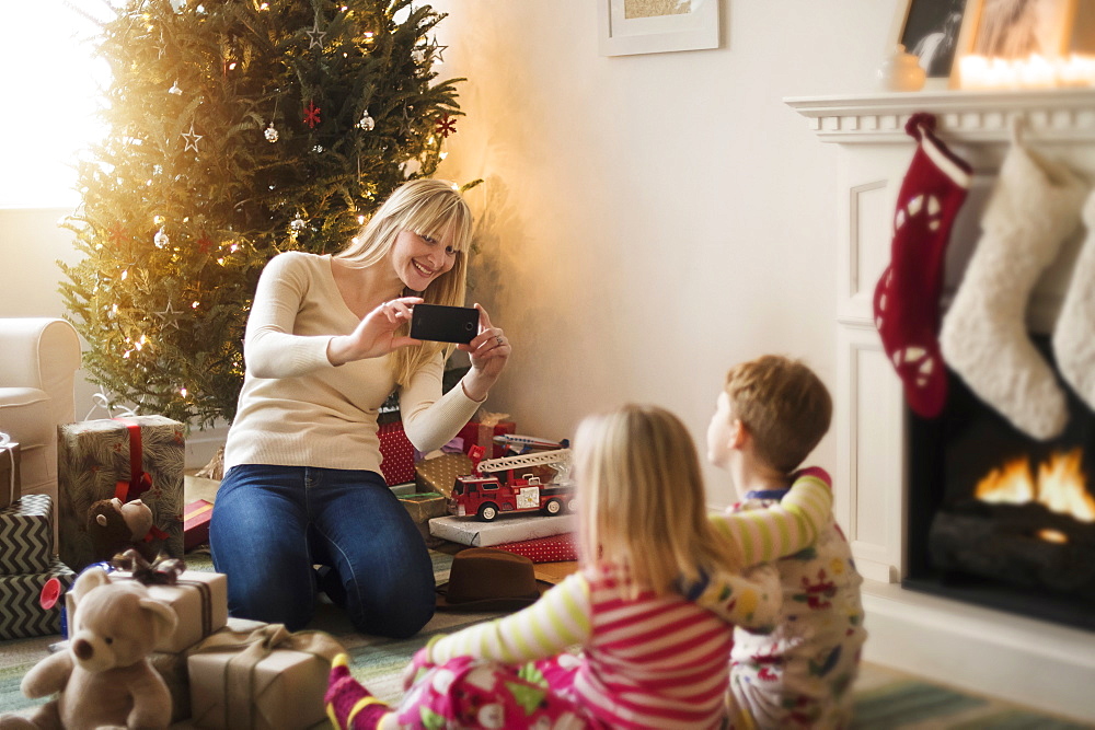 Mother with children (4-5, 6-7) opening christmas presents and taking photos