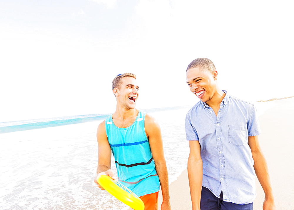 Young man walking and talking, holding plastic disc on beach, Jupiter, Florida