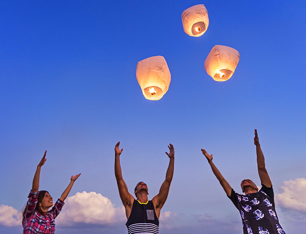 Young people with illuminated lanterns at sunset