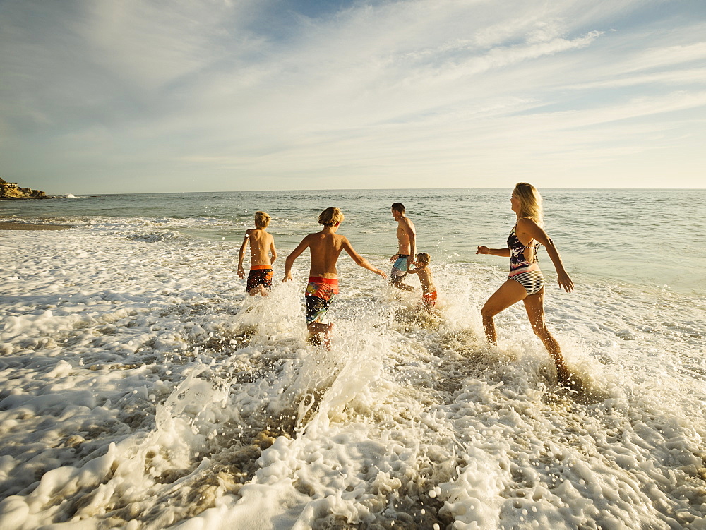 Family with three children (6-7, 10-11, 14-15) running on beach, Laguna Beach, California