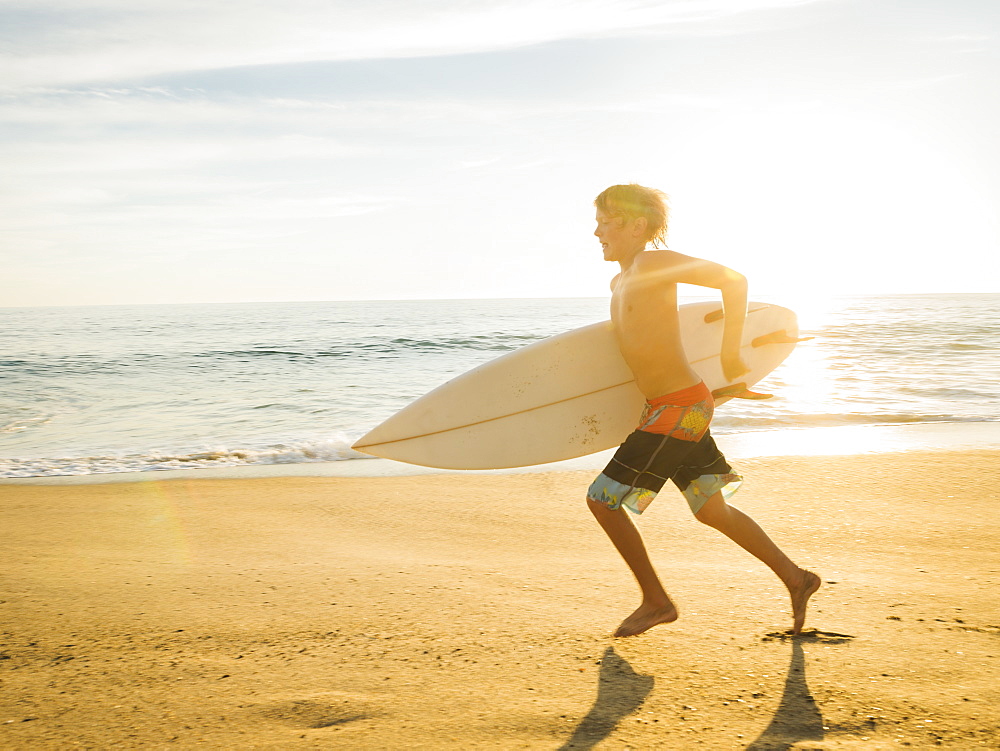 Teenage boy (14-15) with surfboard running on beach, Laguna Beach, California