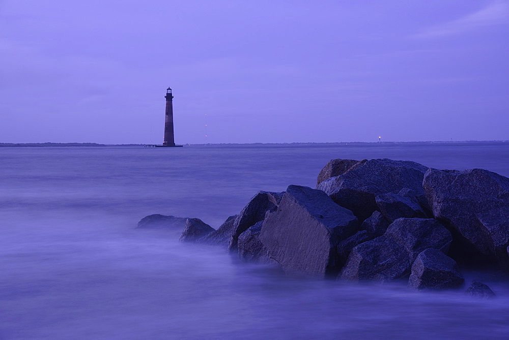 Coastal rocks and lighthouse silhouetted as dusk, Morris Island Light, Folly Beach, South Carolina