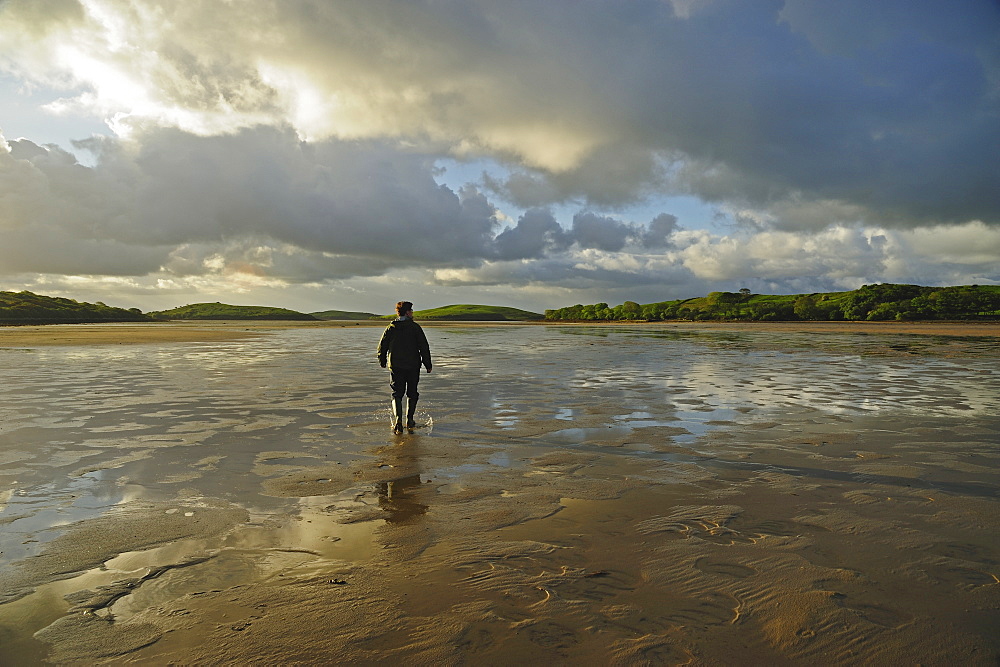 Rear view of man standing water in rubber boots, clouds in sky, Clew Bay, County Mayo, Ireland