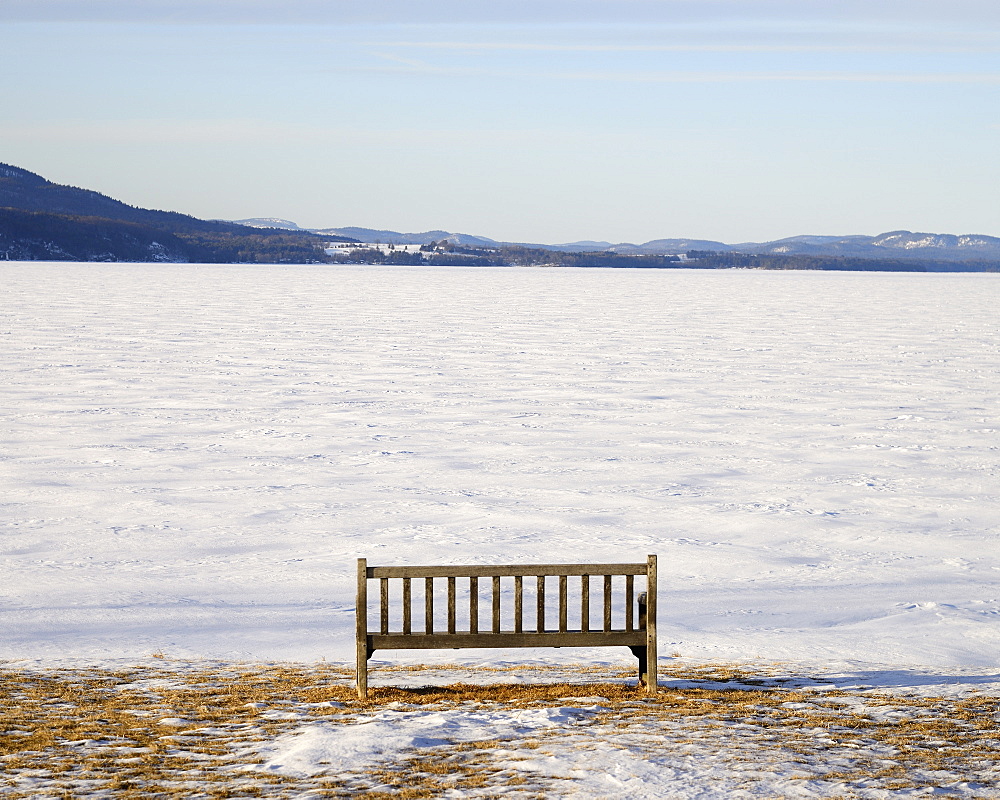 Park bench at edge of a frozen snowed lake, hills in background, Crown Point, New York 