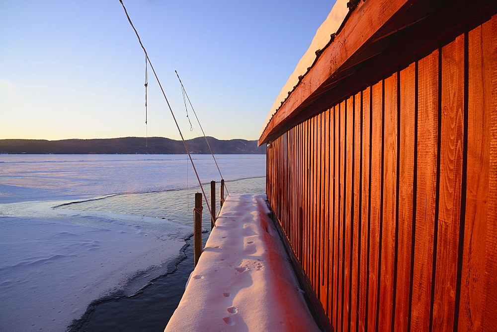 Red Boat House and snow covered pier at edge of lake, Lake George, New York