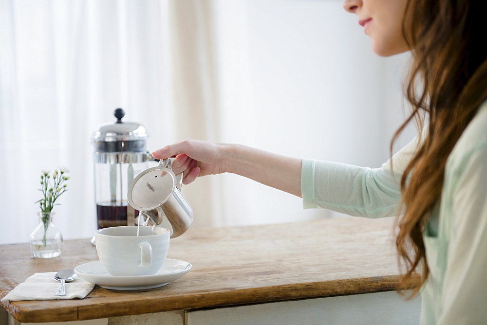 Young woman pouring milk into coffee cup