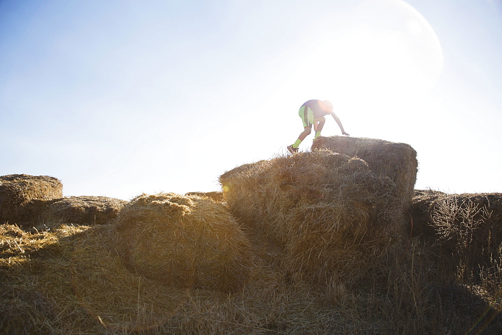 Boy (6-7) climbing on bale of hay