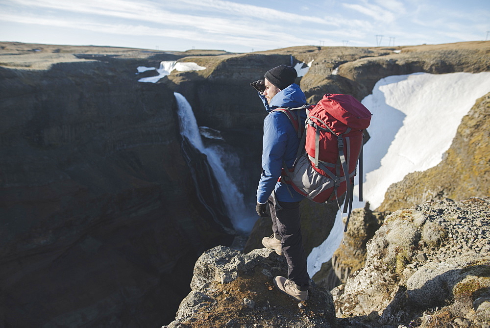 Hiker with backpack on cliff by Haifoss waterfall in Iceland